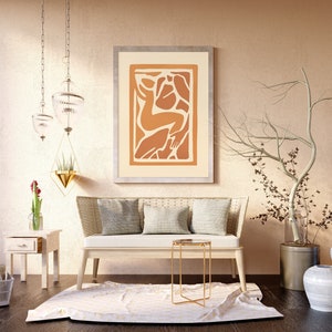 May include: A living room interior design with a white couch, a gold side table, and a framed abstract art print with orange and brown colors. There are two white ceramic vases with a dried branch in a metal vase.