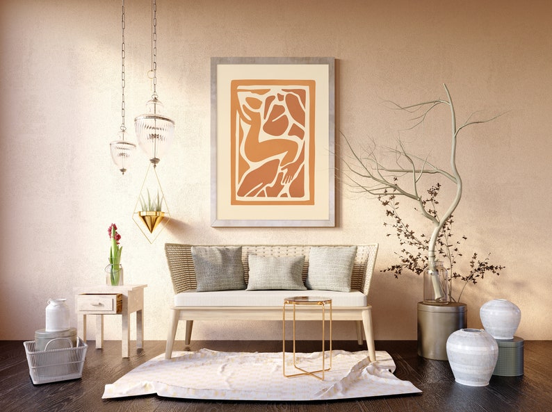 May include: A living room interior design with a white couch, a gold side table, and a framed abstract art print with orange and brown colors. There are two white ceramic vases with a dried branch in a metal vase.
