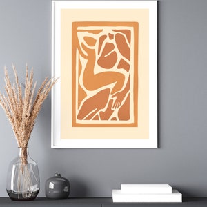 May include: A framed print of an abstract art piece featuring a stylized human figure in shades of orange and brown against a cream background.