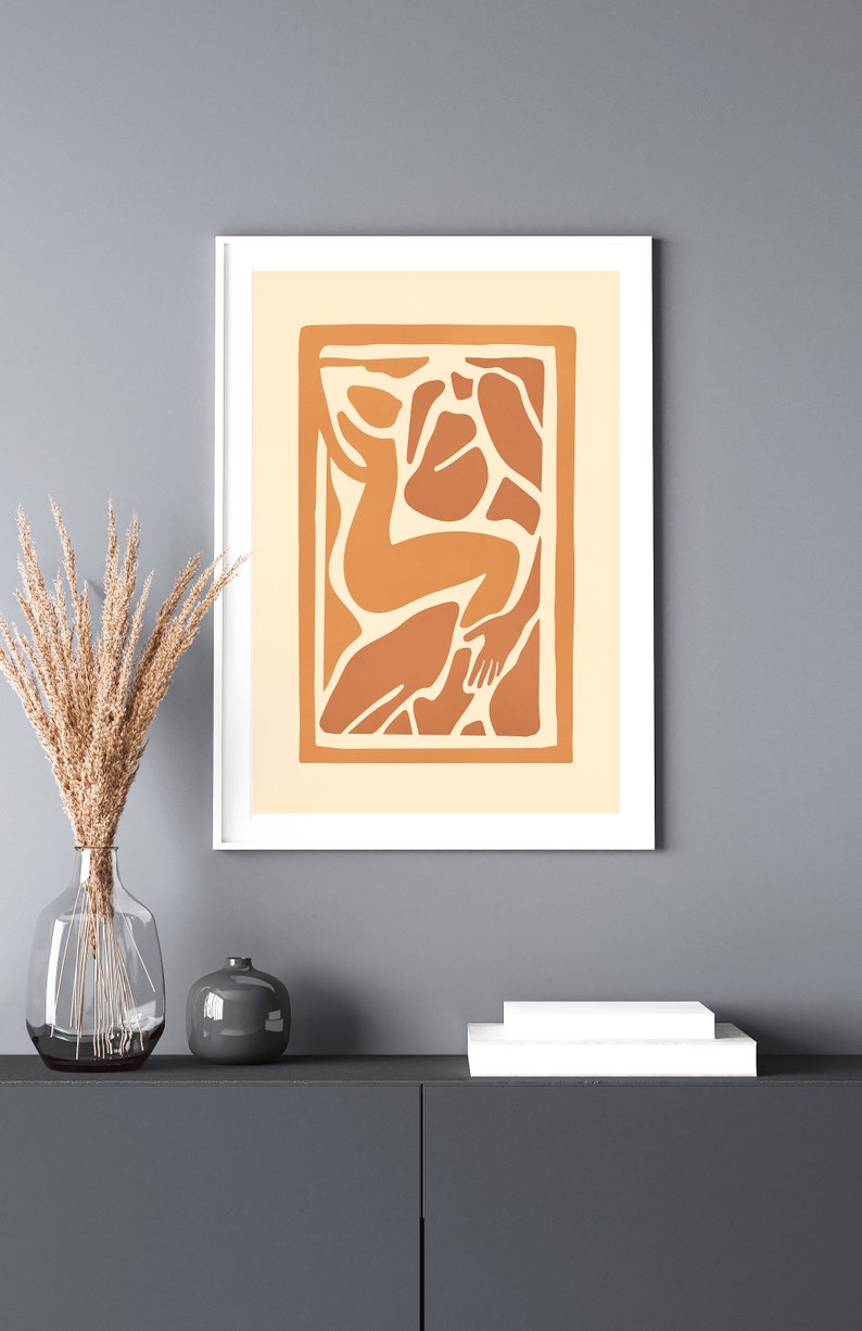 May include: A framed print of an abstract art piece featuring a stylized human figure in shades of orange and brown against a cream background.