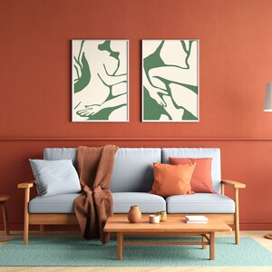 Op de afbeelding: Een woonkamer met een lichtblauwe bank, twee groene abstracte kunstprints, een houten salontafel, een bruin plaid en een staande lamp met een witte kap.