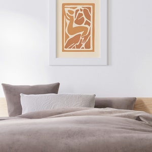 May include: A framed print of an abstract art piece featuring a stylized human figure in shades of orange and brown against a cream background.