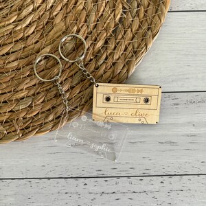 May include: Two keyrings. One is a wooden cassette tape with the names "luca & olive" and a Spotify code. The other is a clear acrylic cassette tape with the names "liam & sophie" and a Spotify code. Both have silver chains.