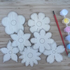 May include: A craft kit with wooden flower shapes, a red paintbrush, and paint pots in assorted colours. The flower cutouts have black outlines and are ready for painting and decorating.