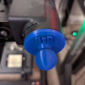 May include: A blue 3D-printed component with the letters "BSD" on a circular base, connected to a spherical ball. The component is attached to a black metal structure. The image is taken from a low angle.