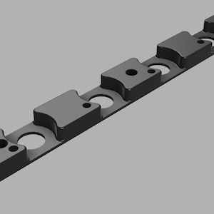 May include: A black, rectangular component with raised, rounded sections and circular cutouts. The component has a matte finish and appears to be made of a solid material. It is designed with several holes and is likely a structural part.
