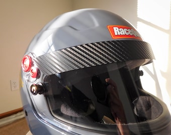 Può includere: Un casco da corsa grigio con una visiera in fibra di carbonio e un adesivo rosso RaceQuip sulla parte superiore.