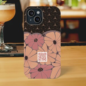 May include: A black phone case with a geometric pattern and pink floral design. The case has a built-in camera lens cover and a QR code.