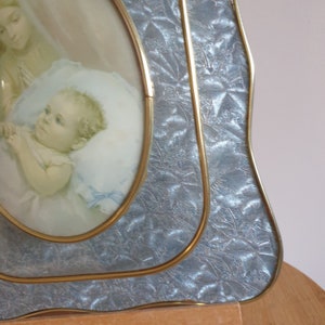 Op de afbeelding: Een vintage ovale fotolijst met een gouden rand en een zilvergrijze, textuurrijke achtergrond. De lijst bevat een foto van een moeder en kind.