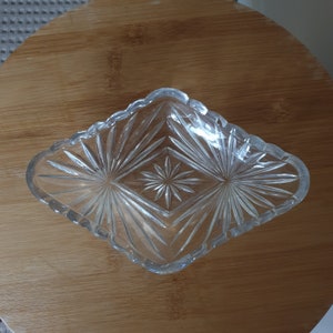 May include: A clear glass dish with a diamond-shaped pattern. The dish has a scalloped edge and is ideal for serving snacks or small treats.