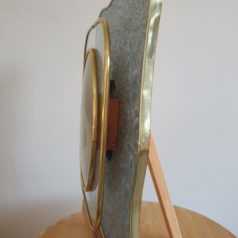 Op de afbeelding: Een gouden fotolijst met een decoratieve, gestructureerde, grijze achtergrond. De lijst heeft een afgeschuinde rand en een standaard aan de achterkant.