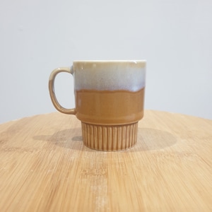 May include: A brown and white ceramic mug with a ribbed base. The mug has a two-tone glaze, with a light brown top and a darker brown bottom.