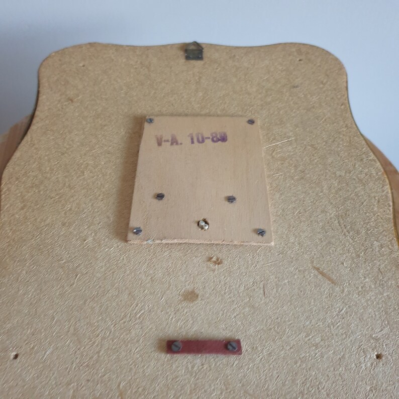 Op de afbeelding: De achterkant van een spiegel in een houten lijst met een label met de tekst "V-A. 10-80".