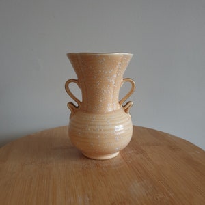 May include: A pale yellow ceramic vase with two handles and a speckled glaze. The vase has a rounded body and a flared opening.