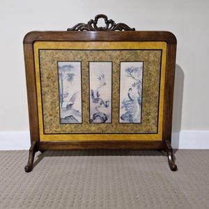 May include: A wooden framed screen with three panels featuring blue and white bird paintings. The frame has a dark brown finish with a decorative top and gold-coloured accents. The screen stands on two legs.
