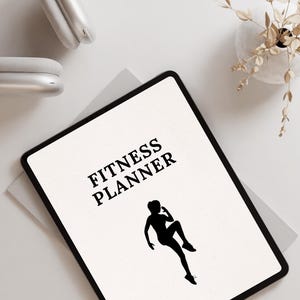 May include: A white tablet with a black border displaying a fitness planner with a silhouette of a person exercising. The text "FITNESS PLANNER" is displayed in black on the tablet.