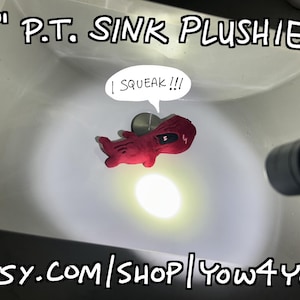 Peut inclure: Un jouet en peluche rouge d'environ 15 cm flotte dans un évier blanc. Le jouet a un œil noir et une bulle de dialogue avec le texte "I SQUEAK!!!". Le texte "6" P.T. Sink Plushie!" est au-dessus de l'évier. L'URL de la boutique Etsy est en bas.