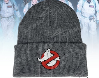 Op de afbeelding: Grijze gebreide beanie met een rode cirkel en een witte geest met een verbodssymbool in het midden. De beanie heeft een omslag.