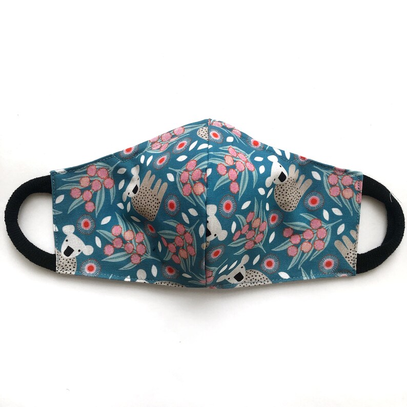 May include: A teal blue face mask with a repeating pattern of pink flowers and white koalas. The mask has black elastic ear loops.