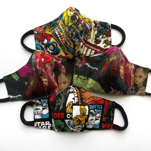 Op de afbeelding: Vier verschillende stoffen mondmaskers met verschillende superhelden- en stripfigurenontwerpen. De maskers zijn zwart, rood, blauw en groen met afbeeldingen van personages zoals Iron Man, Hulk en Darth Vader.