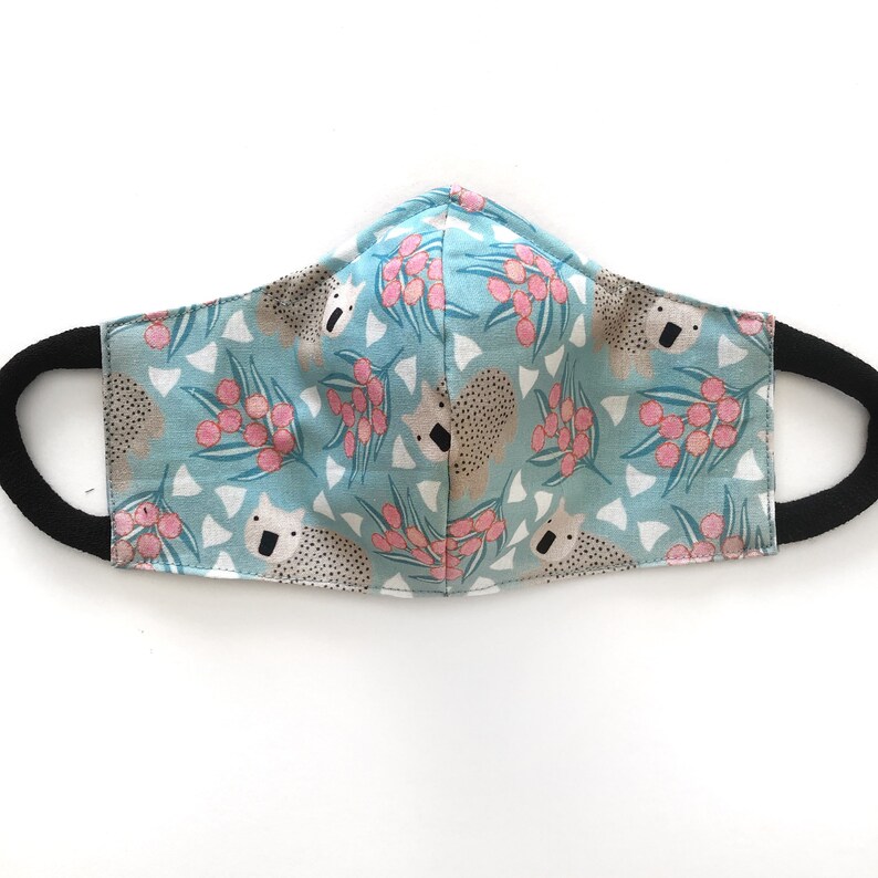 May include: A blue face mask with a repeating pattern of koalas and pink flowers. The mask has black elastic ear loops.
