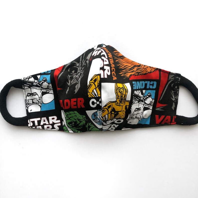 Op de afbeelding: Een zwart, rood, blauw en geel stoffen mondkapje met een Star Wars-thema. Het masker bevat personages en tekst uit de Star Wars-franchise, waaronder Darth Vader, C-3PO, R2-D2, en de woorden "Star Wars" en "Vader".