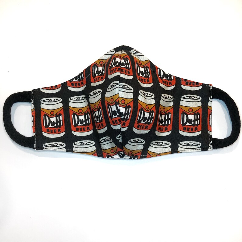 Op de afbeelding: Zwart gezichtsmasker met een herhalend patroon van rode en witte Duff Beer-blikjes. De blikjes hebben de tekst "Duff Beer" erop gedrukt.