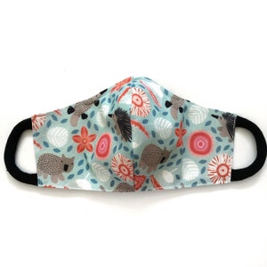 May include: A turquoise blue face mask with a repeating pattern of wombats, echidnas, and flowers. The mask has black elastic ear loops.