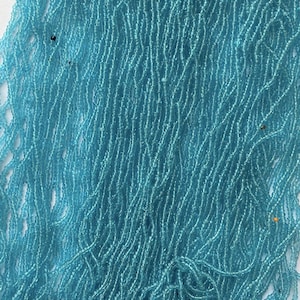 Peut inclure: Un grand paquet de perles de rocaille en verre bleu clair. Les perles sont petites et rondes, et elles sont enfilées sur un fil fin.