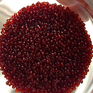 May include: A small glass bowl filled with a large quantity of small, dark red glass beads.