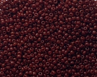 May include: A close-up shot of a large pile of small, round, dark red beads. The beads are scattered across a white surface. The beads are uniform in size and shape, with a small hole running through the center of each one. These beads are ideal for jewelry making.