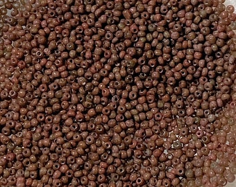 May include: A close-up view of a bowl filled with small, round, brown seed beads. The beads are arranged in a circular pattern, creating a uniform and dense texture.