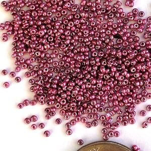Op de afbeelding: Een stapel kleine, ronde, metallic roze kralen verspreid op een wit oppervlak. Een Amerikaanse dime-munt ligt naast de kralen ter vergelijking van de grootte. De munt toont het profiel van Franklin D. Roosevelt en de woorden "Liberty" en "In God We Trust."