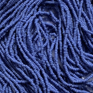 May include: A close-up of a pile of small, round, blue glass beads. The beads are all the same size and shape, and they are arranged in a random pattern.