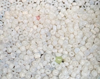 May include: A close-up of a large quantity of small, white, iridescent glass beads. The beads are round with a small hole in the center.