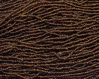 May include: A close-up of a strand of brown seed beads. The beads are small and round, and they are arranged in a random pattern. The beads are made of glass and have a shiny finish.