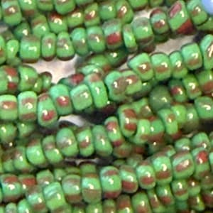 May include: Close-up of green and red glass beads strung together. The beads are a light green colour with a darker red stripe around the middle. The beads are cylindrical and appear to be handmade, with slight variations in shape and colour.