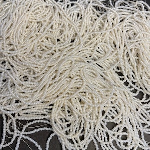 Puede incluir: Un montón grande de cuentas de semillas blancas. Las cuentas son pequeñas y redondas, y están dispuestas en un patrón aleatorio.