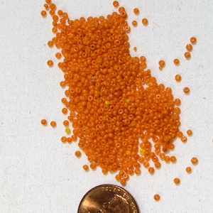 Puede incluir: Un montón grande de pequeñas cuentas de vidrio naranja, esparcidas sobre una superficie blanca. Un céntimo de euro se incluye para la escala.