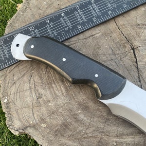May include: A black and silver knife with a black handle and a silver blade. The knife is on a wooden surface.