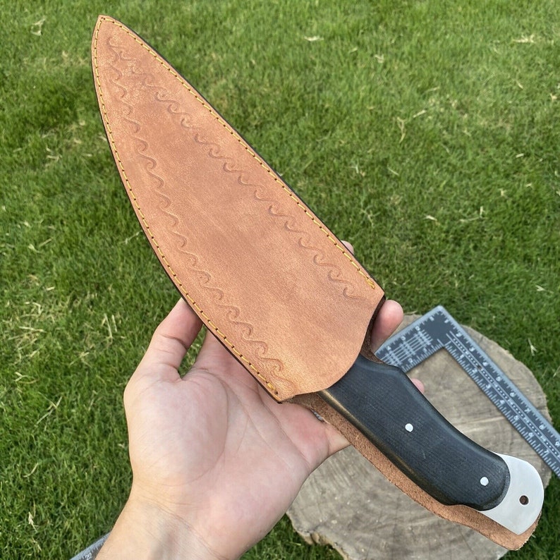 May include: A brown leather knife sheath with a wave pattern and yellow stitching. The knife has a black handle and a silver blade.