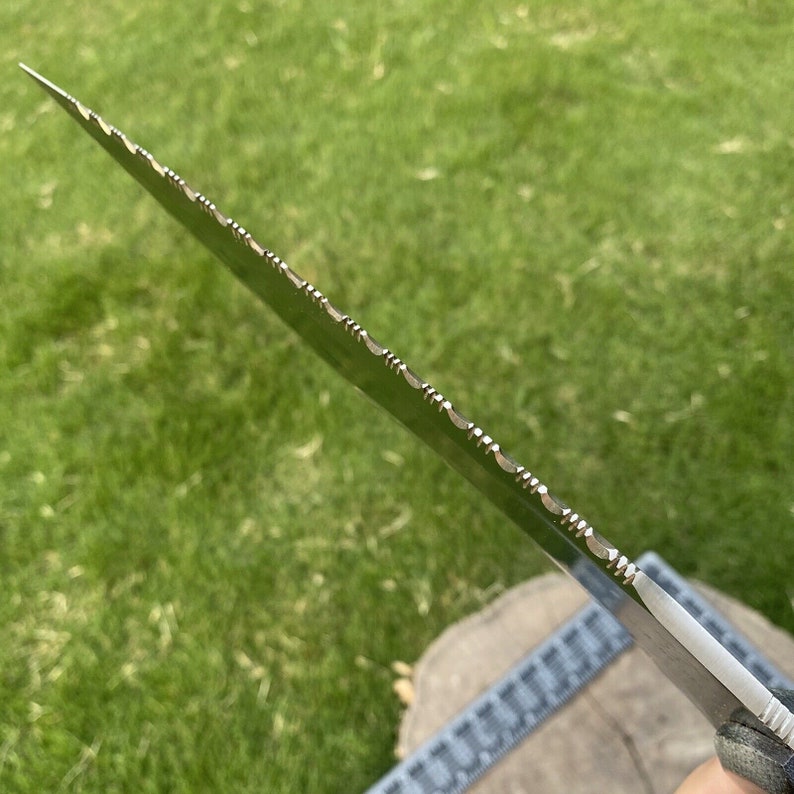 May include: Close-up of a serrated knife blade with a silver finish. The blade has a series of small, evenly spaced teeth along the edge.