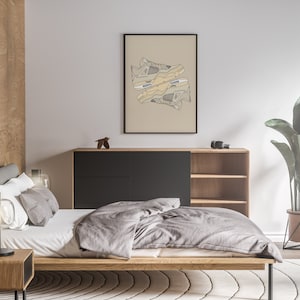 May include: A bedroom interior featuring a bed, a bedside table, a lamp, a chest of drawers, a plant, and a framed print of a pair of trainers. The print is in a minimalist style with a beige background and black lines.