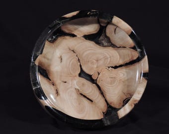 May include: A wooden bowl with a black resin rim. The bowl is made from a light-colored wood with a unique grain pattern. The resin rim is smooth and polished.
