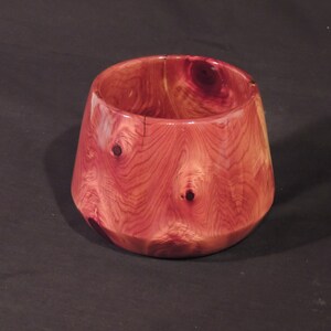May include: A handcrafted wooden bowl with a reddish-brown hue. The bowl has a wide, slightly flared shape with a flat base and a smooth, polished finish. The wood grain and knots are visible, adding to its natural aesthetic.
