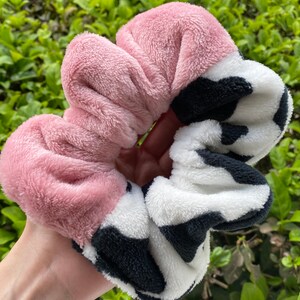 May include: A pink and white fuzzy scrunchie with a black cow print design.