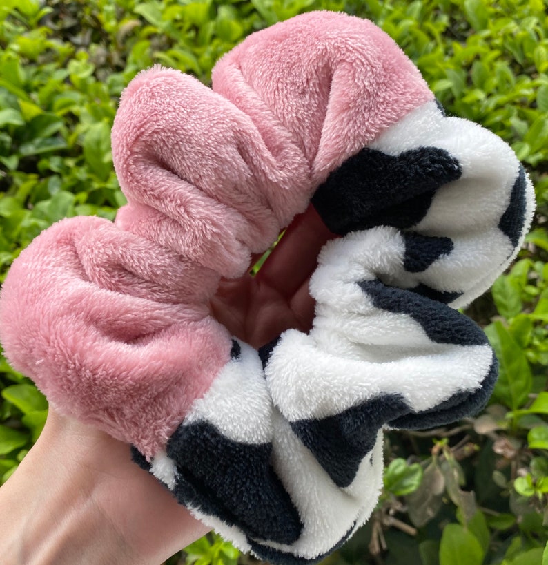 May include: A pink and white fuzzy scrunchie with a black cow print design.