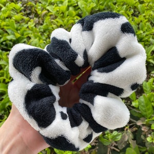 May include: A black and white cow print scrunchie made of soft, fluffy fabric.