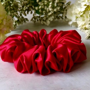 May include: A bright red satin scrunchie for hair. The scrunchie is made of soft, silky fabric and is designed to be gentle on hair.
