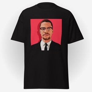 May include: Black t-shirt featuring a portrait of a man in a suit and glasses against a red background. The graphic is a stylized illustration with a focus on the subject's face and attire. The shirt is a classic crew neck.